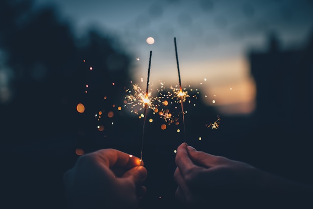 Sunset image with two hands holding lit sparklers to celebrate